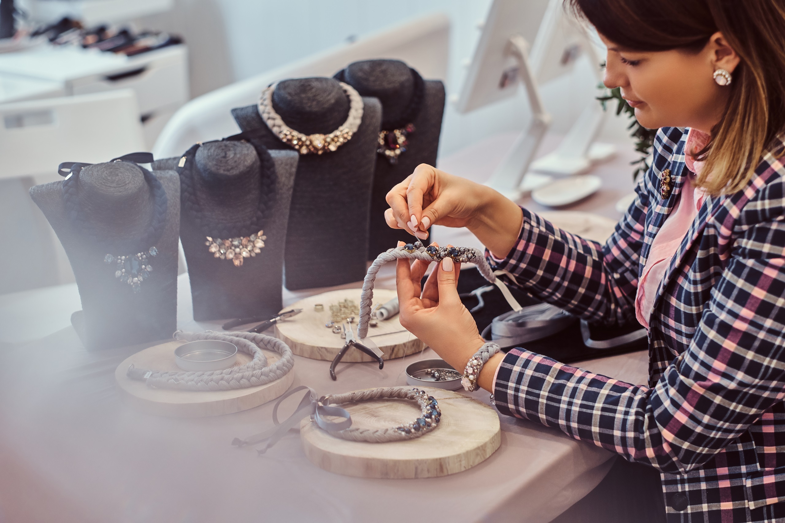 Elegantly dressed woman makes handmade necklaces, working with needles and thread in jewelry workshop.